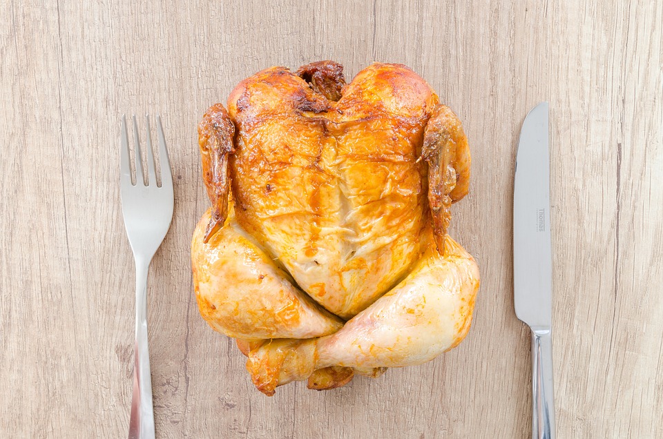 whole roasted chicken on wooden table with silverware