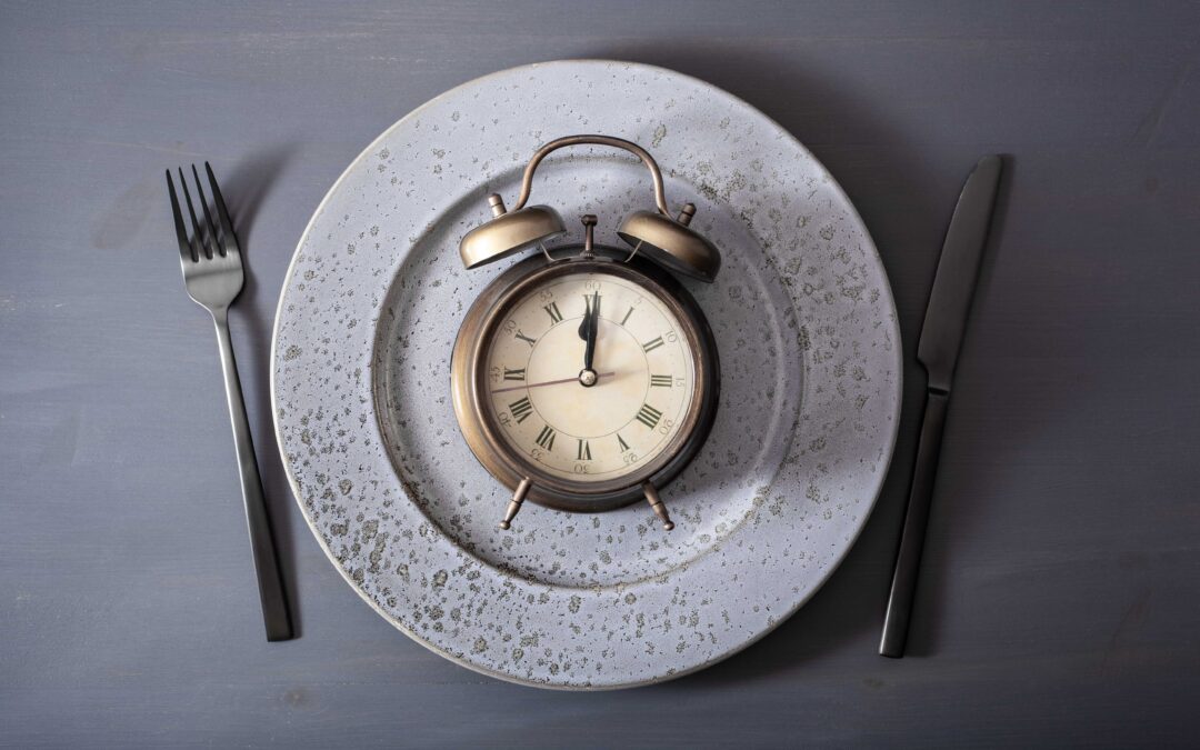 Alarm clock sitting on a speckled plate between a fork and a knife