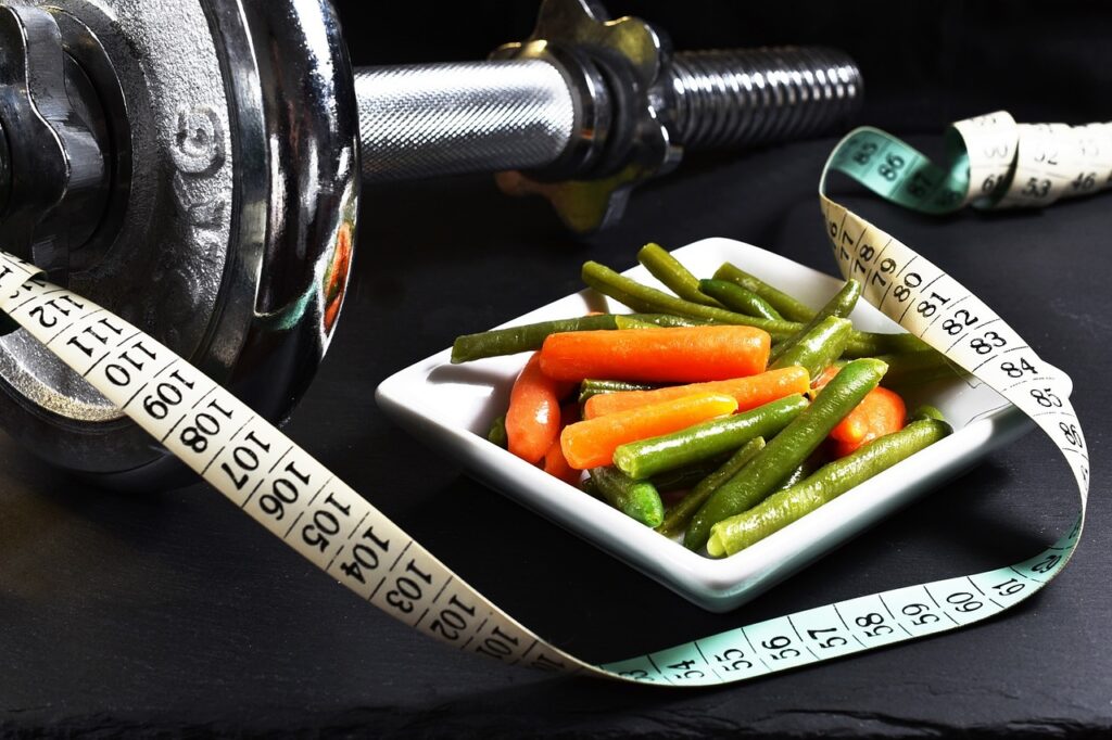 close up of barbell weight and dish of cooked carrots and green beans with a measuring tape wrapping around