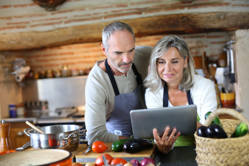 older couple cooking in kitchen and looking at smart device