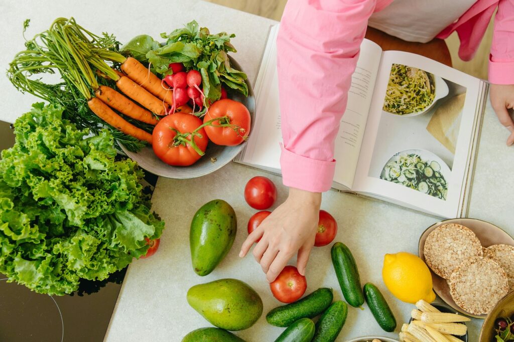 kitchen counter top showing healthy vegetables and woman's arm grabbing tomato