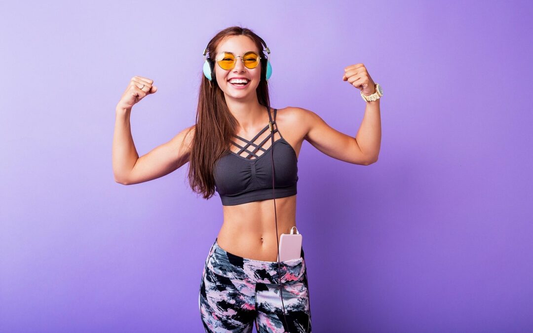 younger woman in workout clothes and headphone flexing infront of purple background